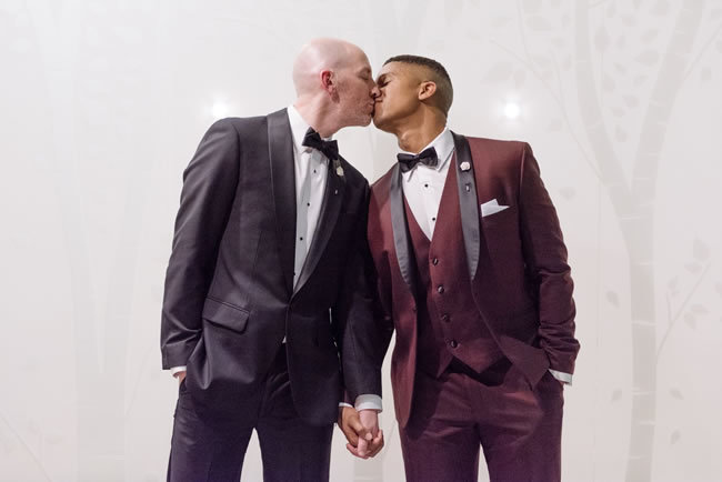 Two grooms in snazzy tuxedos share a kiss