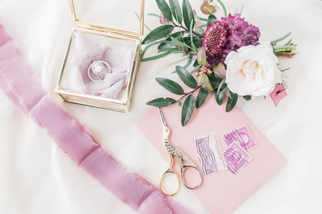 Wedding rings, flowers, and stationery in plum tones