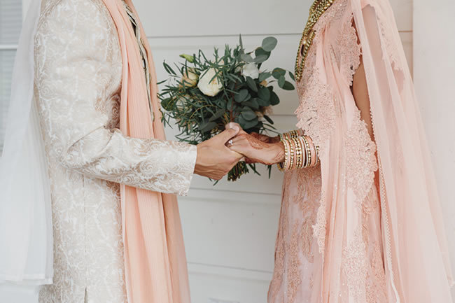 Indian bride and groom in peach attire holding hands