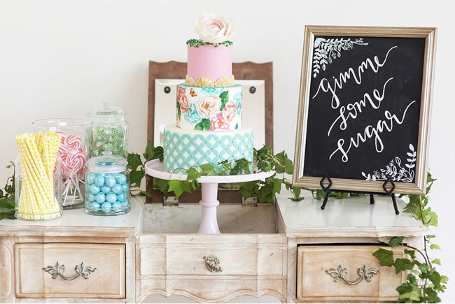 A colorful wedding cake with a 'Gimme Some Sugar' chalkboard sign