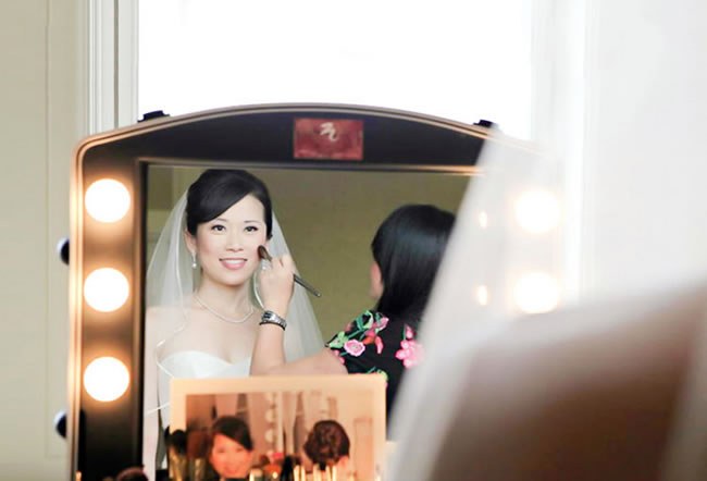 Asian bride in front of a mirror getting her wedding makeup done