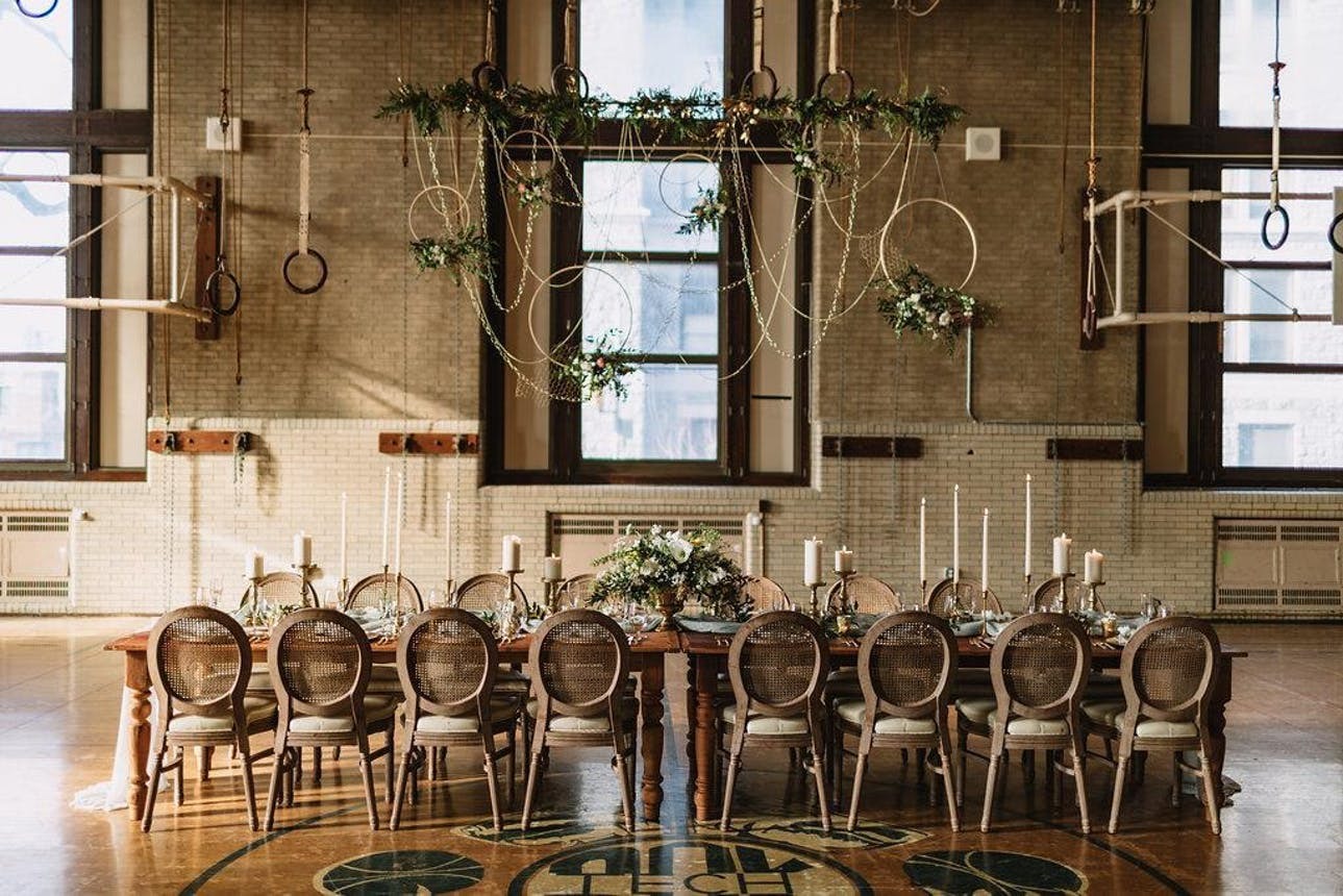 A school gym converted into a contemporary wedding reception space with a family-style table and overhead décor installations