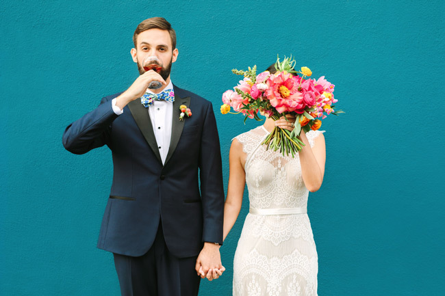 Quirky wedding couple pose in front of teal wall | Find a wedding photographer that fits your style