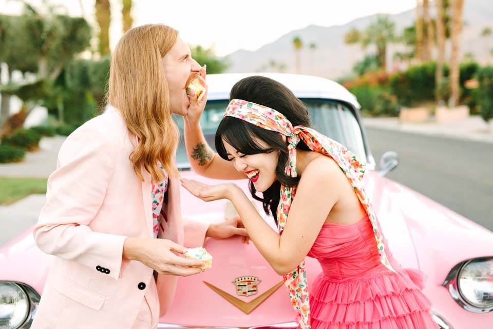 How To Plan Wedding Budget | A bride and groom in bright pink laugh as they feed each other wedding cake